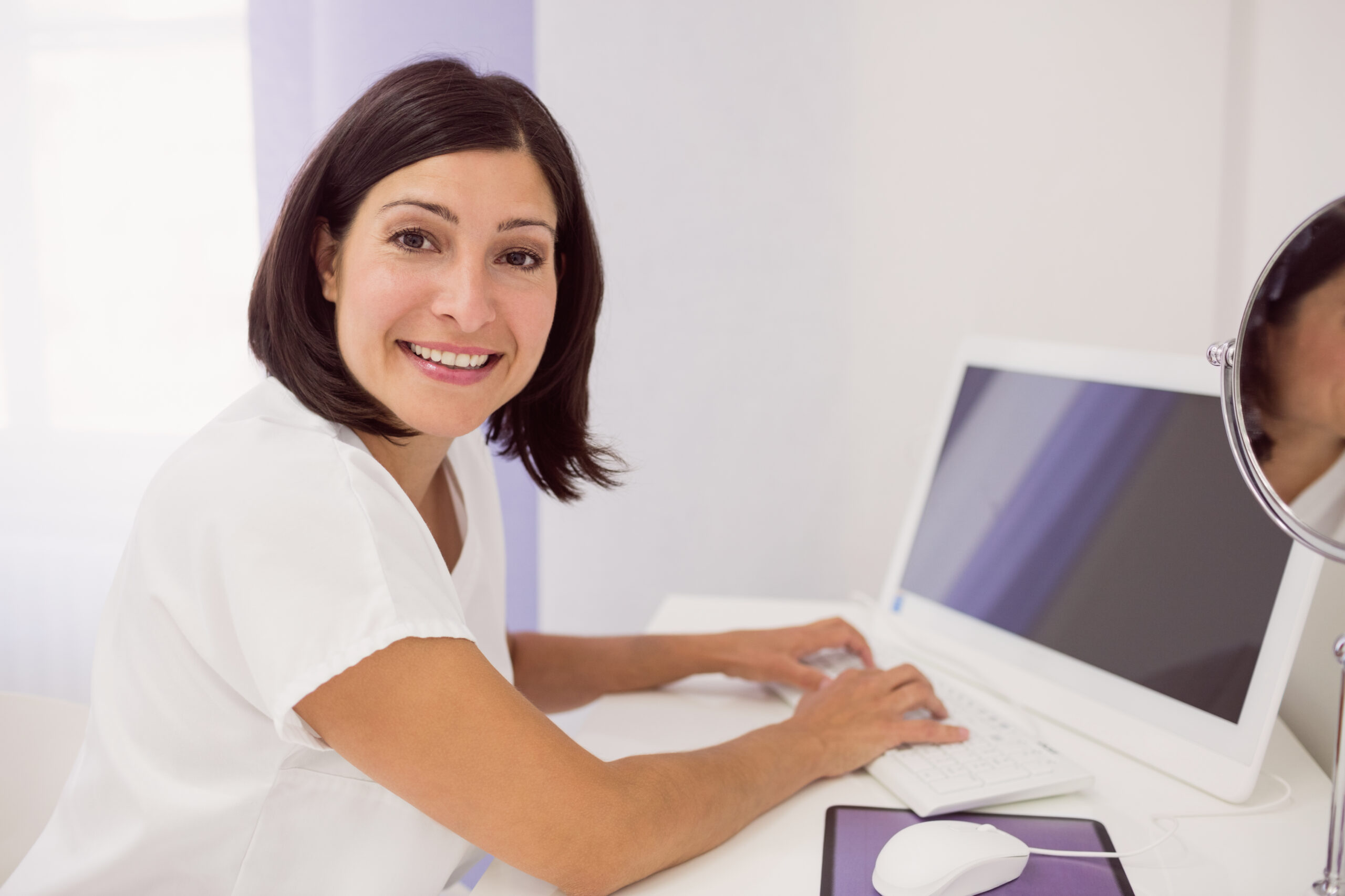 Clinic staff member smiling while working at a desktop computer in a Brooklyn salon