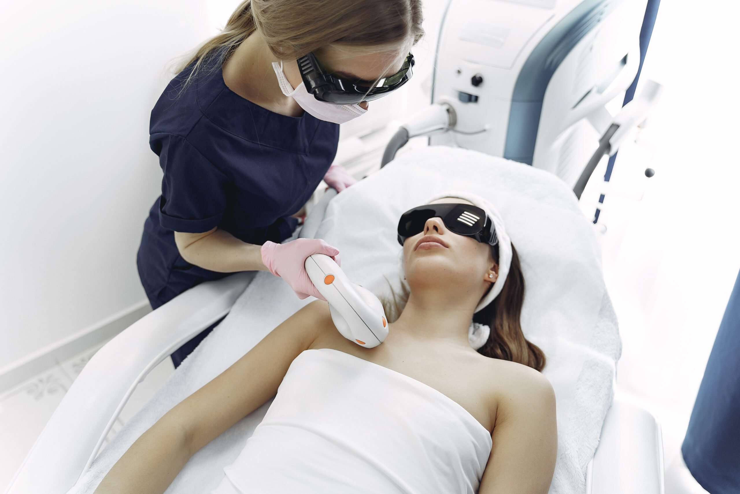 Technician in scrubs and protective eyewear performing laser hair removal with proper safety equipment in a Brooklyn clinic