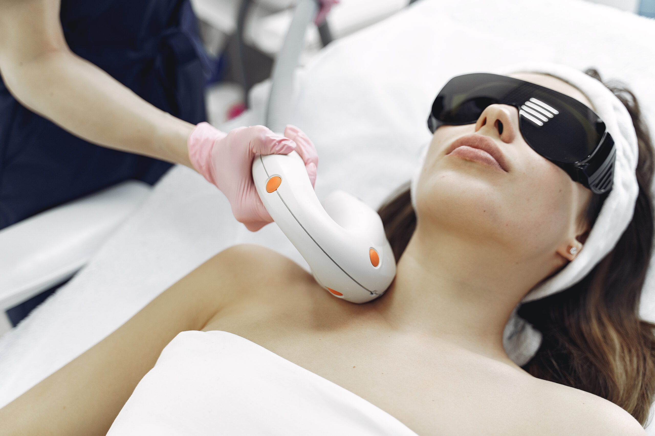 Technician using a laser device on a client's neck and collarbone area with eye protection at a Brooklyn clinic