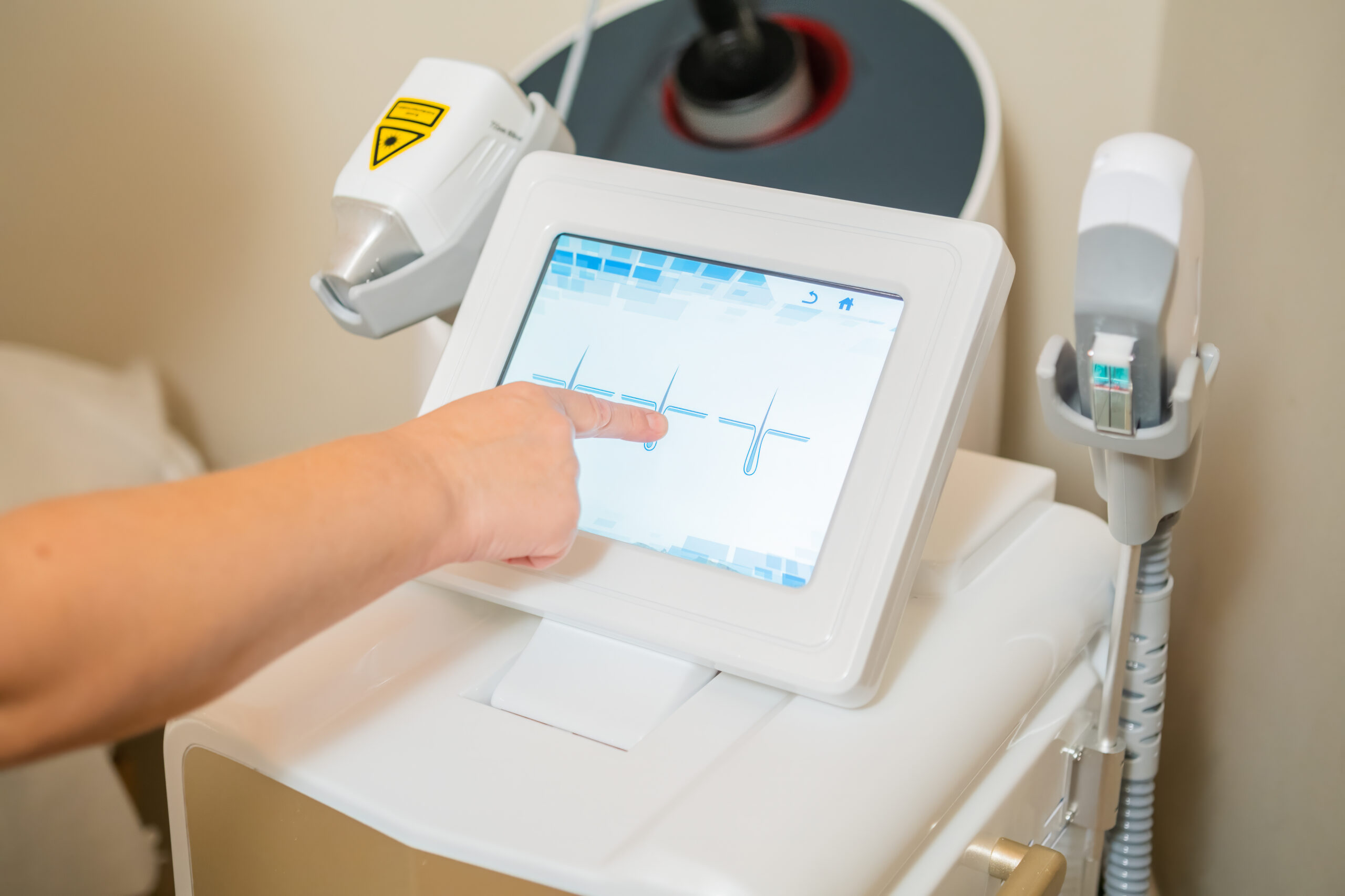 Technician adjusting settings on a laser hair removal device touchscreen at a Brooklyn clinic