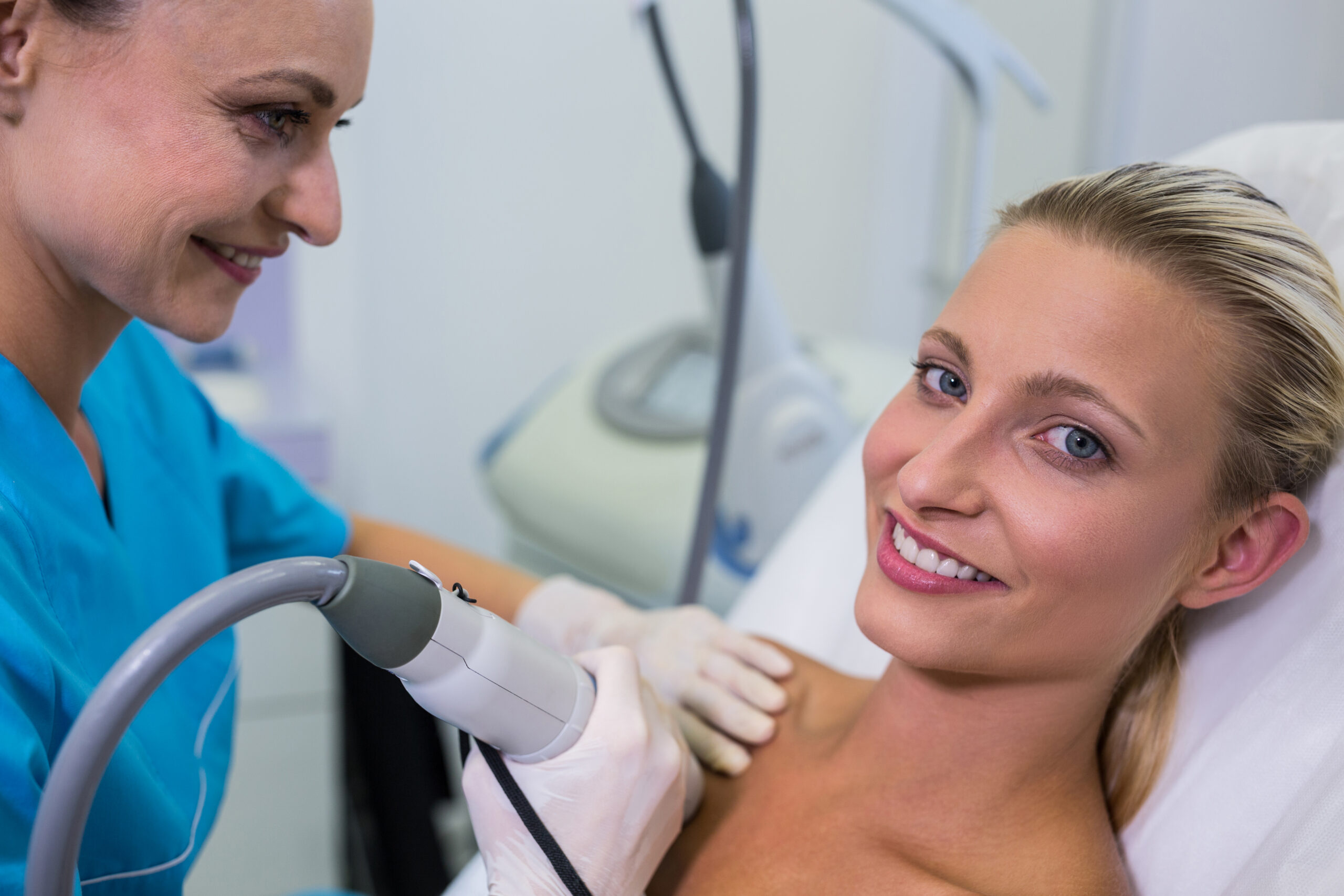Technician in gloves performing laser hair removal treatment on a client's shoulder in a Brooklyn clinic