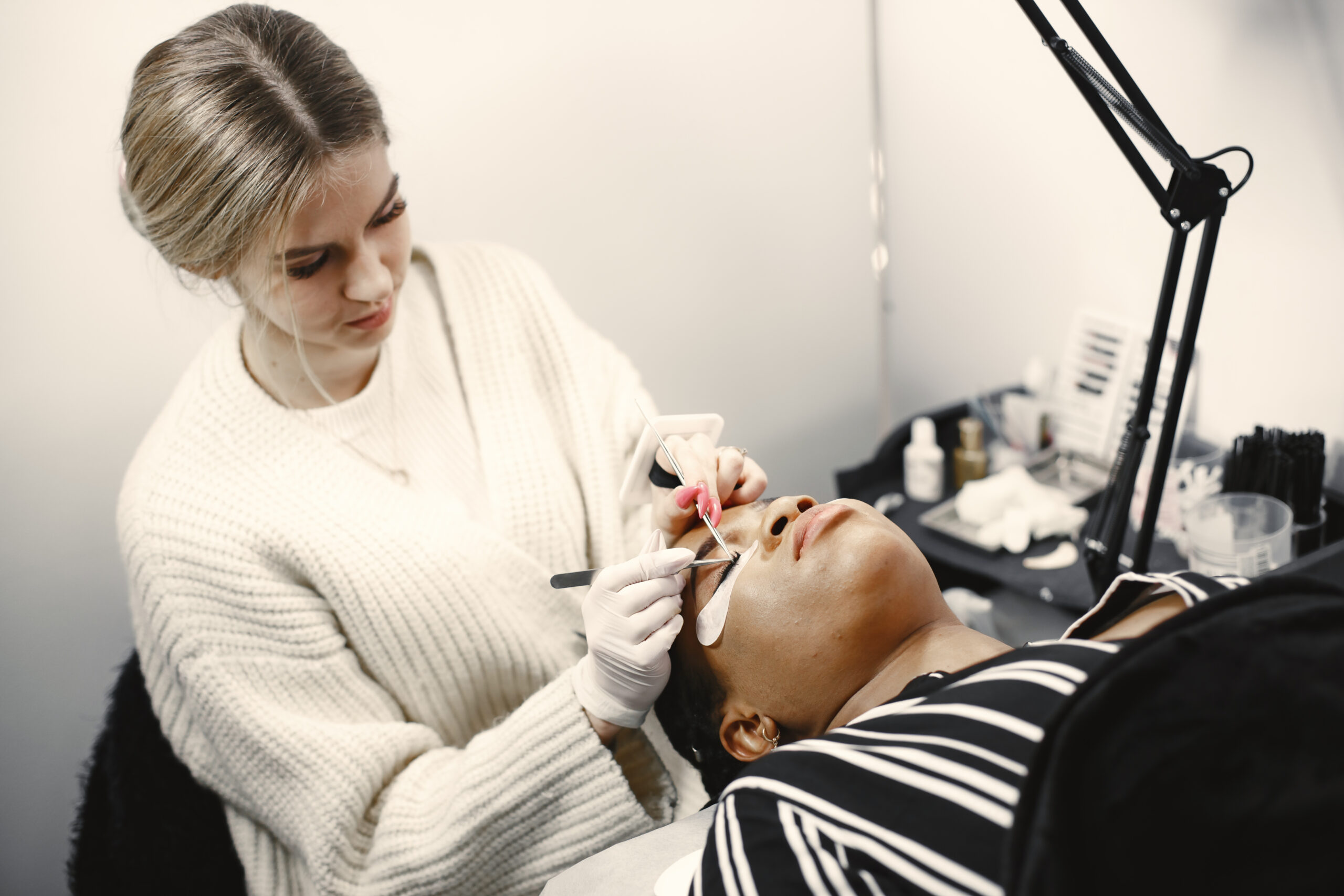 Causes of lash extensions falling out early, lash technician working in treatment room